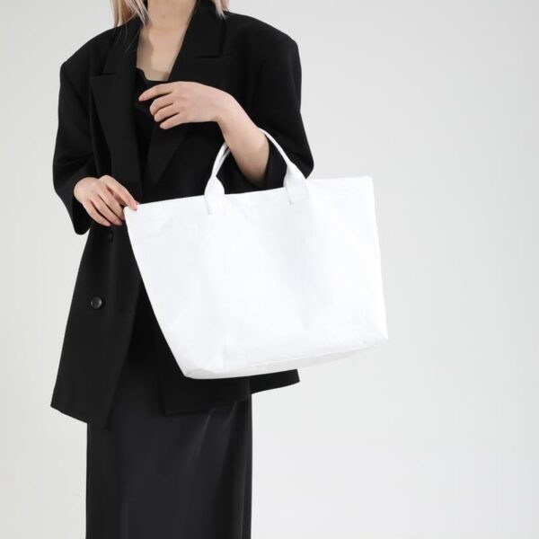 White DuPont Paper Tote Bag Manufacturer Guide: MOQ 500, 20–25 Days Lead Time & Global Delivery for Bulk Travel Bag Orders 1 model wearing a black outfit holding a white tote bag, thumbnail preview with the identifier 4-7-19-6.